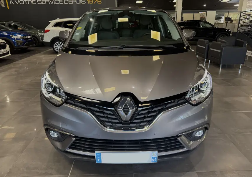 Vue de face d'un Renault Grand Scenic IV Business gris Cassiopée dans un showroom avec éclairage intérieur.
