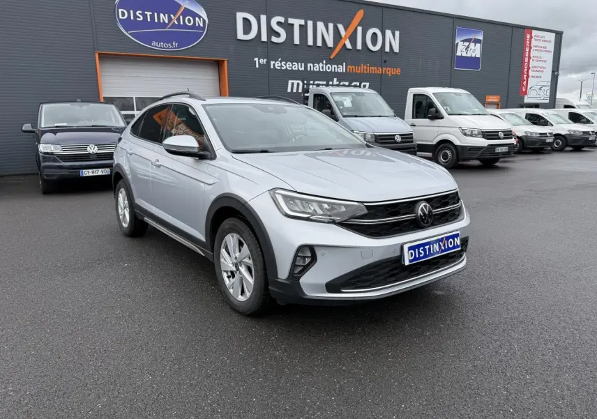 Volkswagen Taigo gris reflet d'argent métallisé vu en 3/4 avant droit sur parking de concession multimarque.