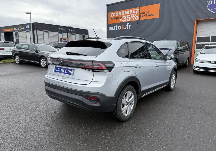 Vue 3/4 arrière droite d'un Volkswagen Taigo gris reflet d'argent métallisé sur parking de concession.