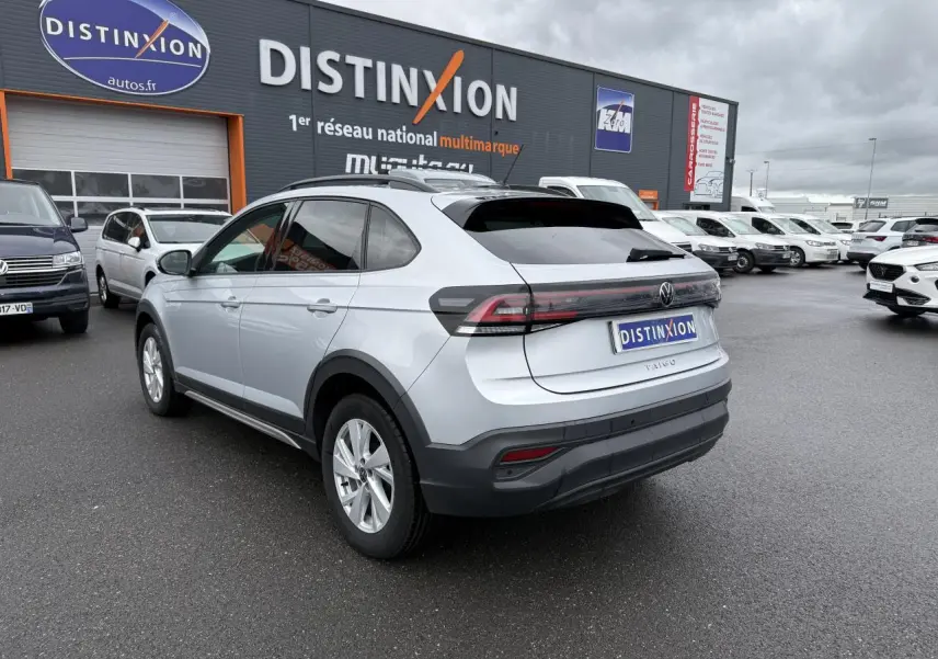 Vue 3/4 arrière droite d'un Volkswagen Taigo gris reflet d'argent métallisé stationné devant un concessionnaire Distinxion.