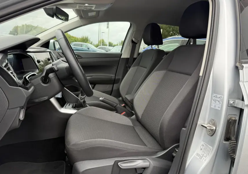 Intérieur avant droit du Volkswagen Taigo gris reflet d'argent, sièges tissu gris et volant cuir multifonctions visible.