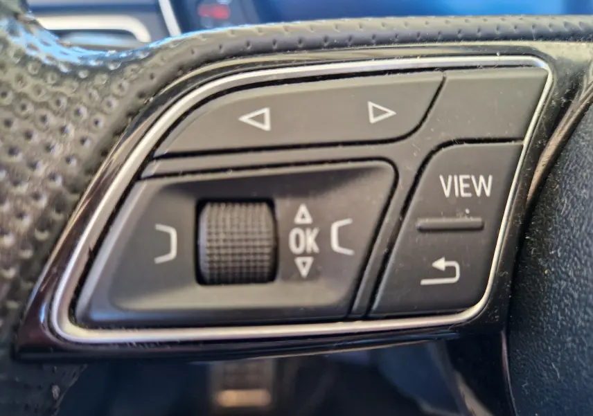 Gros plan sur les commandes noires du volant en cuir perforé de l'Audi A5 Cabriolet 2017, avec boutons multifonctions et molette.