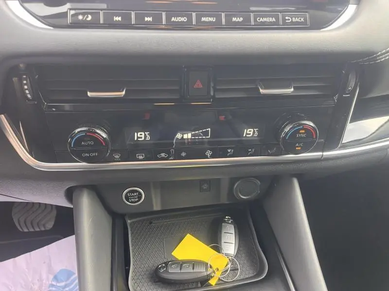 Vue rapprochée de la console centrale du Nissan Qashqai 2022, avec commandes climatisation et clés sur le rangement noir.