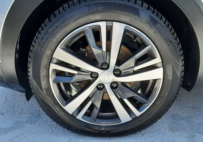 Gros plan sur la roue avant droite du Peugeot 3008 gris Artense avec jante alliage bicolore et logo lion central.