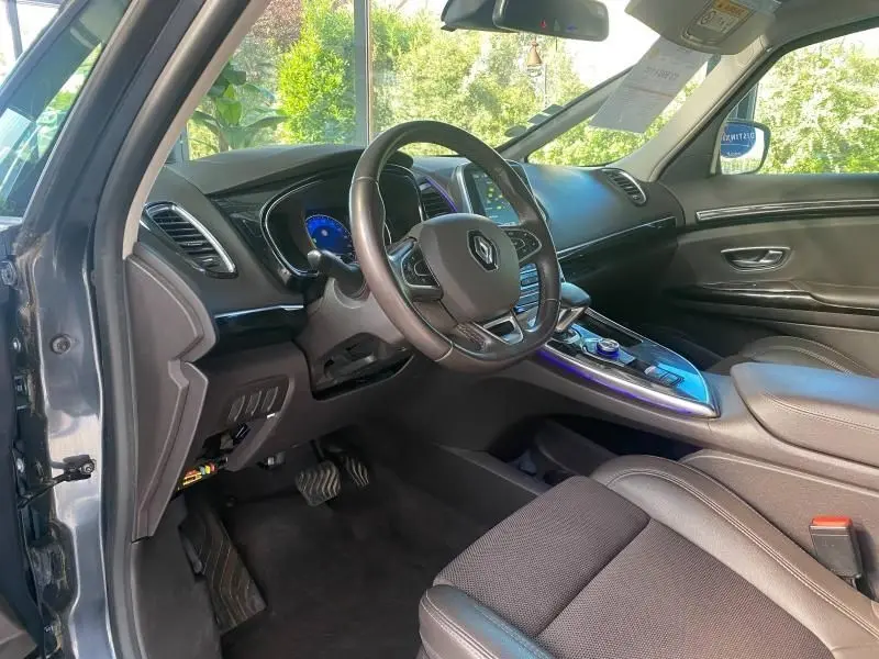 Vue intérieure côté conducteur du Renault Espace V gris, mettant en valeur le volant cuir multifonction et la console centrale avec écran tactile.