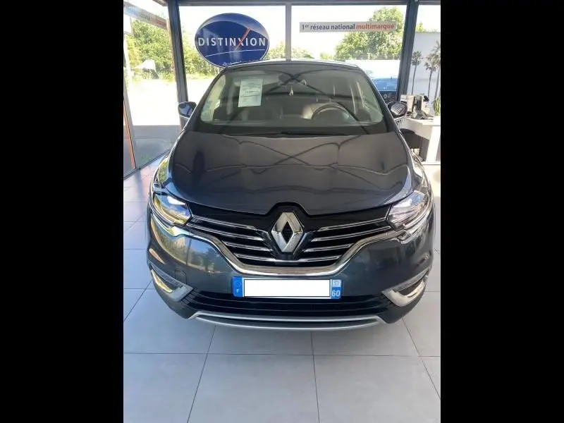 Vue avant d'un Renault Espace V gris exposé en showroom avec calandre chromée et logo central visible.