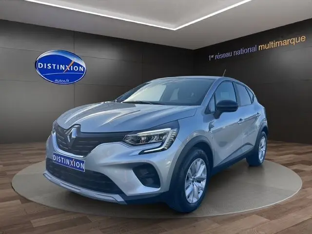Renault Captur TCE 90 Evolution gris Highland en 3/4 avant droit, intérieur showroom avec logo Distinxion visible.