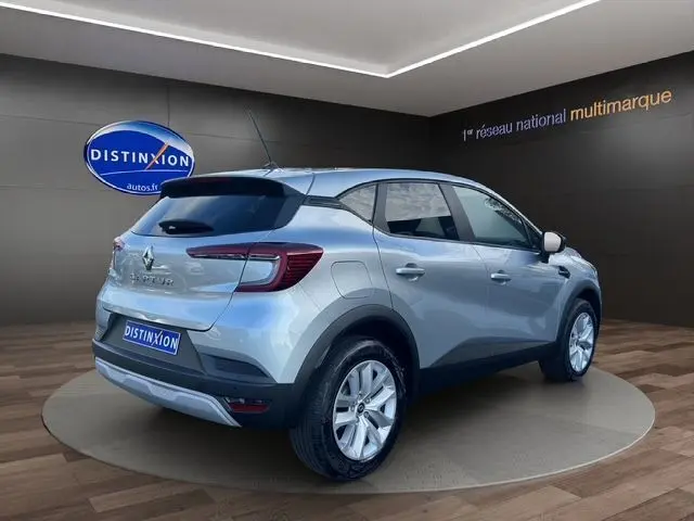 Vue 3/4 arrière droite du Renault Captur TCE 90 Evolution gris Highland, stationné en showroom avec logo Distinxion visible.
