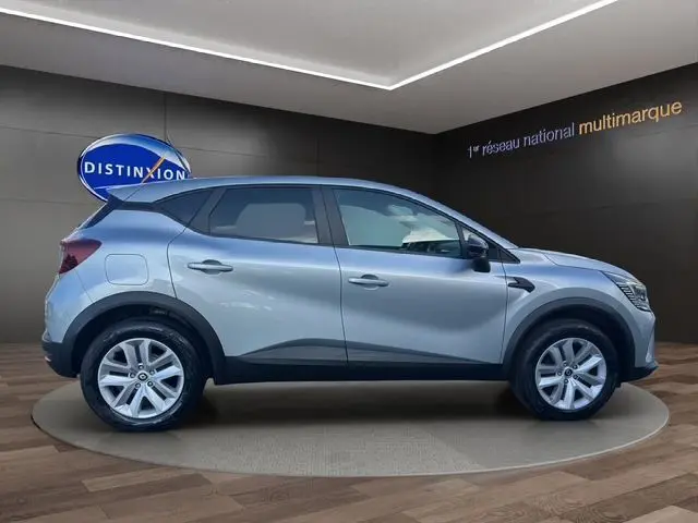 Profil droit d'un Renault Captur TCE 90 Evolution gris Highland 2024 en intérieur showroom, avec jantes alliage et lignes noires contrastantes.