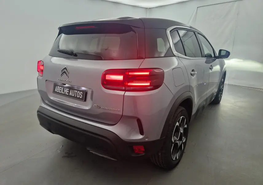 Vue 3/4 arrière droite du Citroën C5 Aircross gris Artense avec feux arrière allumés et toit noir contrastant.