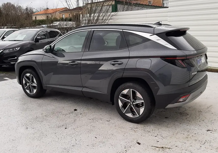 Vue 3/4 arrière gauche d'un Hyundai Tucson 2025 gris Ecotronic avec hayon électrique et jantes bi-ton.