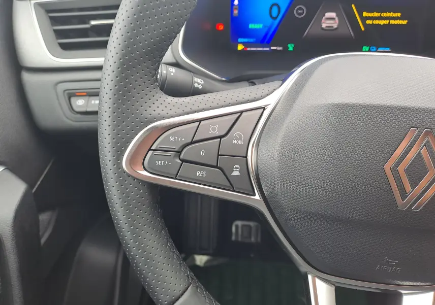 Gros plan sur le volant cuir perforé et les commandes à gauche du tableau de bord numérique d'une Renault Symbioz 2025.