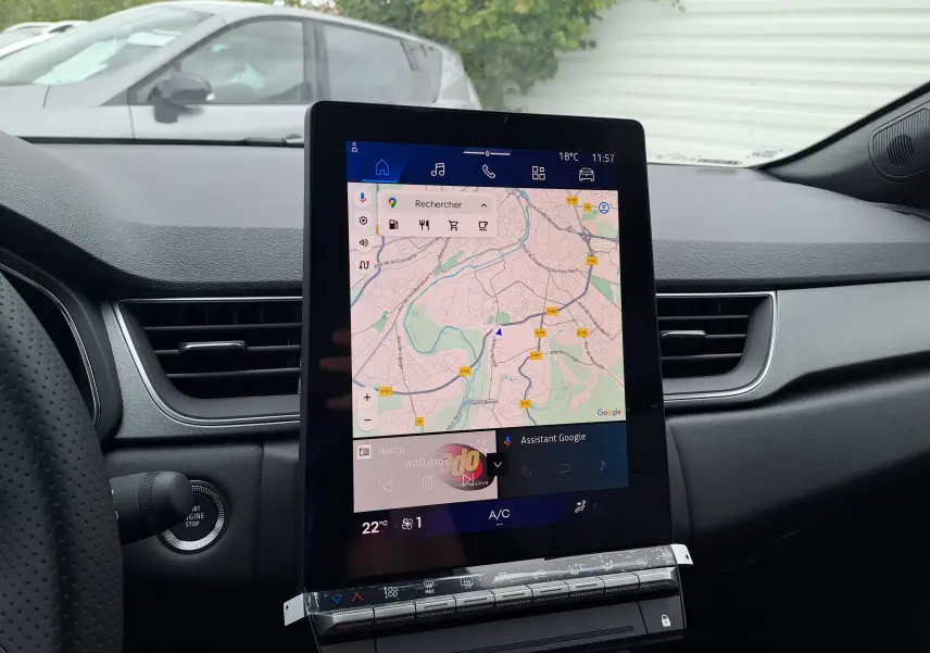 Vue intérieure centrée sur l'écran tactile du tableau de bord d'une Renault Symbioz 2025, avec une voiture grise visible à l'extérieur.