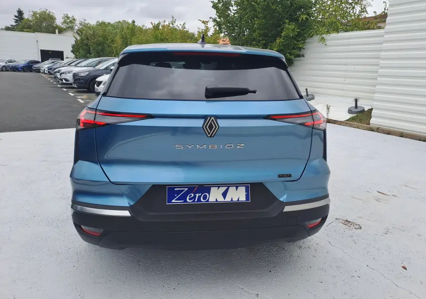 Vue arrière d'un Renault Symbioz bleu mercure avec feux arrière fins et logo central sur un parking extérieur.