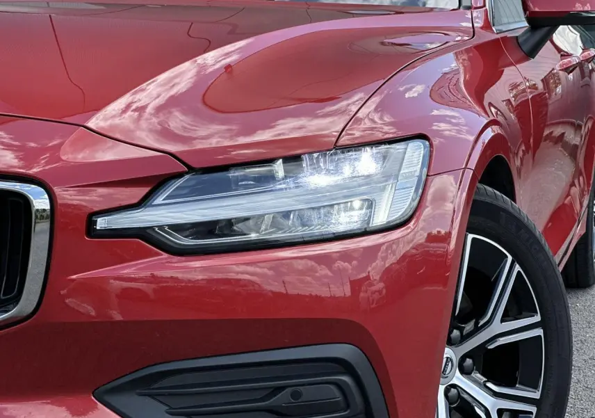 Gros plan sur l'avant droit rouge Fusion d'une Volvo S60 2024, mettant en valeur le phare LED et la jante alliage noire diamant.