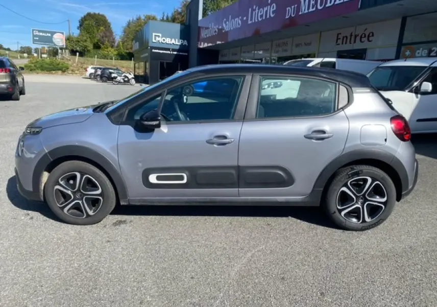 Profil côté gauche d'une Citroën C3 2022 gris Artense avec Airbump noirs et enjoliveurs 3D sur parking extérieur.