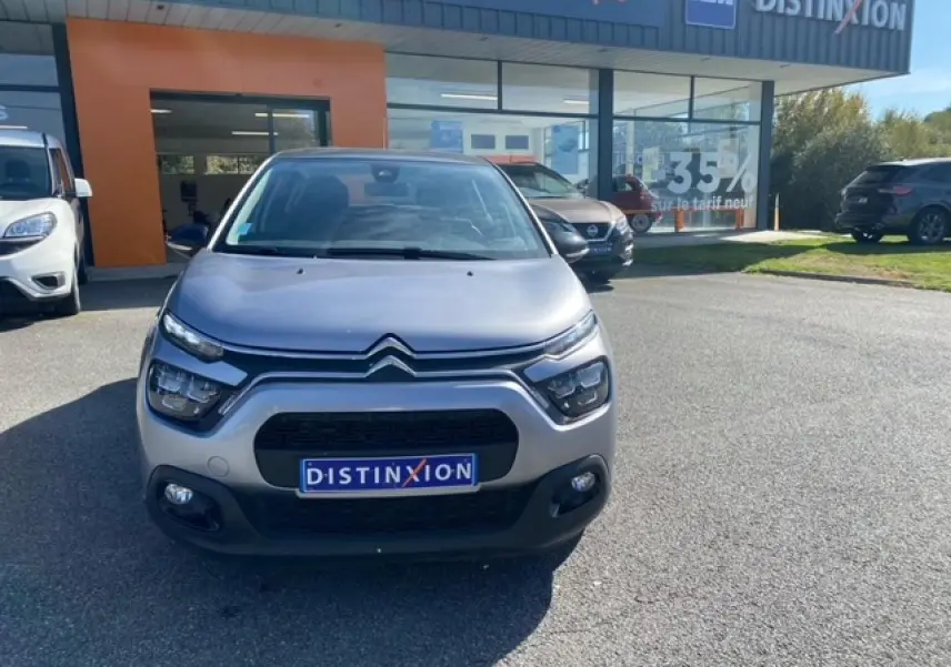 Citroën C3 gris Artense métal vue de face avec calandre noire et feux LED distinctifs au soleil devant un showroom.