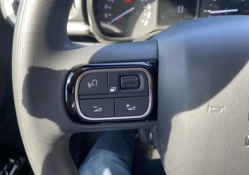 Gros plan sur les commandes du volant d'une Citroën C3 2022 essence, finition Shine, avec boutons de volume et mains libres.