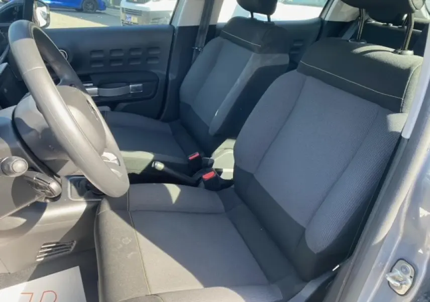 Vue intérieure côté conducteur de la Citroën C3 gris Artense métal, sièges tissu gris et volant noir.