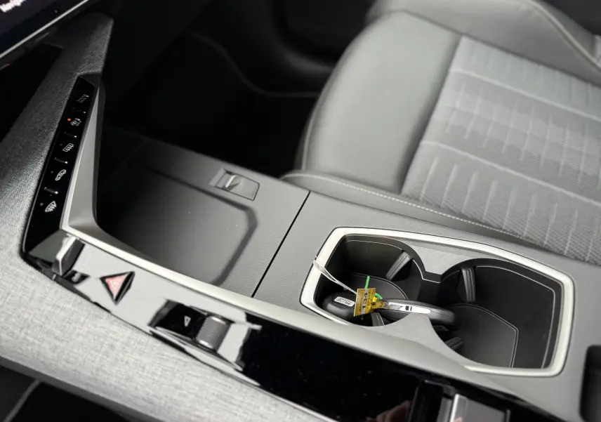 Gros plan sur la console centrale et porte-gobelets du Peugeot 3008 Hybrid 2025 avec sellerie grise et finitions modernes.