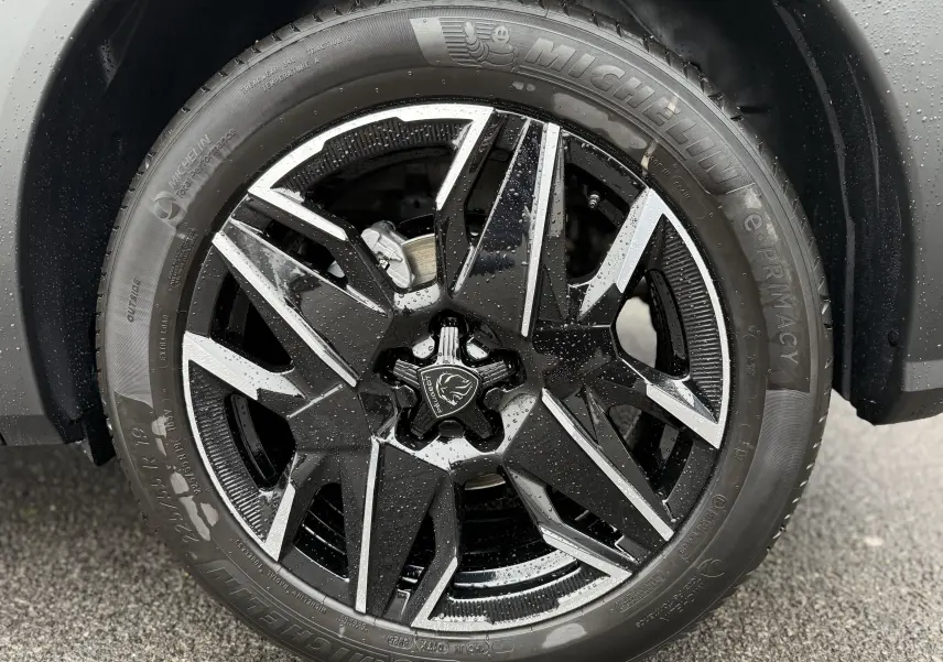 Gros plan sur la jante noire et argentée du Peugeot 3008 Hybrid 2025, avec logo lion au centre et pneus Michelin mouillés.