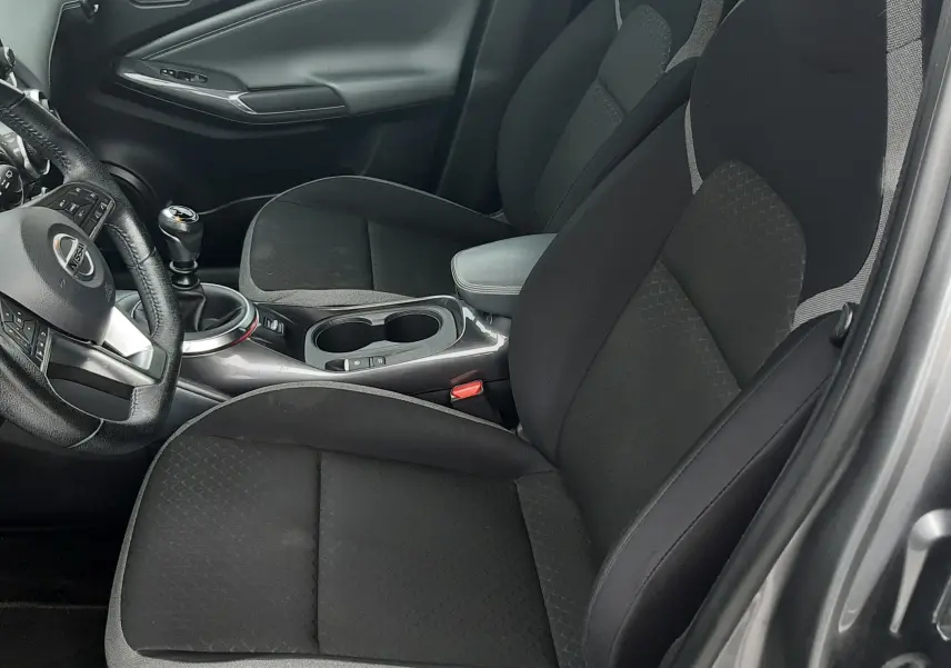 Vue intérieure côté conducteur du Nissan Juke gris 2020, montrant sièges tissu noirs et levier de vitesse manuel.