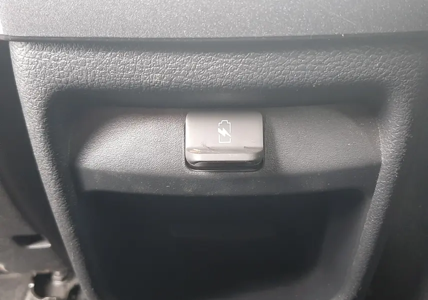 Détail intérieur montrant un bouton de verrouillage de batterie avec symbole éclair sur fond noir texturé.