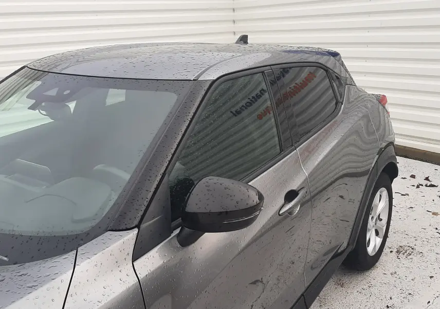 Vue 3/4 avant droit d'un Nissan Juke gris 2020 avec rétroviseur noir et vitres teintées sous la pluie.