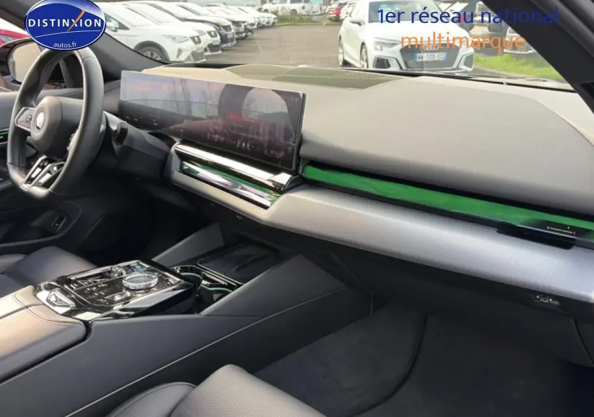 Intérieur BMW Série 5 i5 M60 2024 vu côté passager, tableau de bord moderne avec écran large et inserts verts.