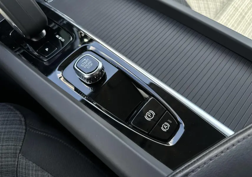 Gros plan sur la console centrale noire brillante de la Volvo S60 B4 197 DCT7 MHEV Core+ avec bouton start/stop et commandes électroniques.