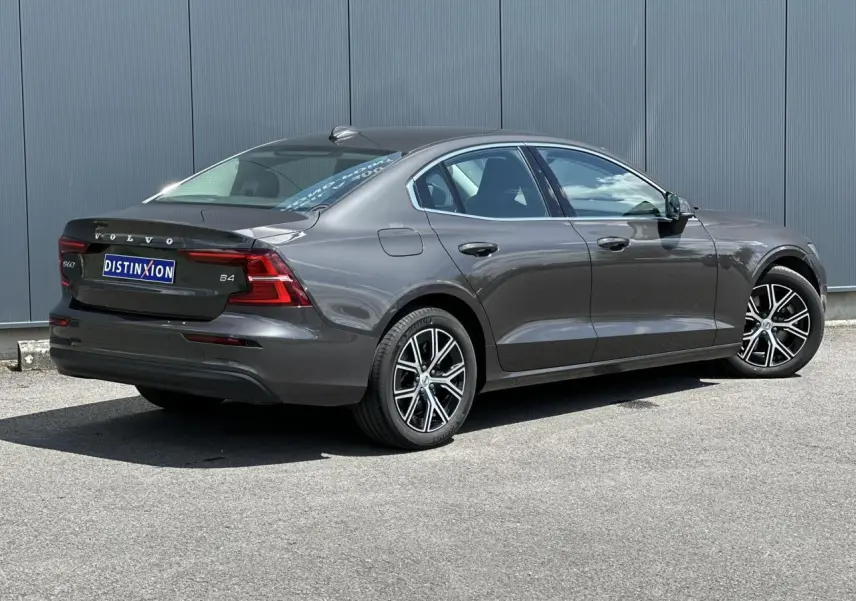 Volvo S60 B4 gris Platinium vue 3/4 arrière droit, jantes alliage noires et feux arrière LED distinctifs.