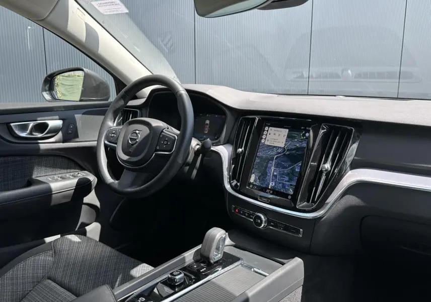 Intérieur avant droit du Volvo S60 2024 avec tableau de bord noir, écran tactile vertical et volant multifonction.