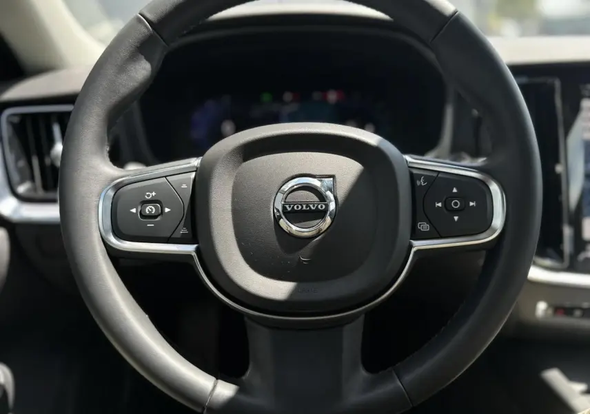 Volant noir de Volvo S60 2024 avec commandes intégrées, cadrans numériques flous en arrière-plan.