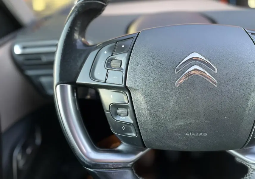 Gros plan sur le volant noir de la Citroën C4 Picasso 2014, avec commandes intégrées et logo chromé au centre.