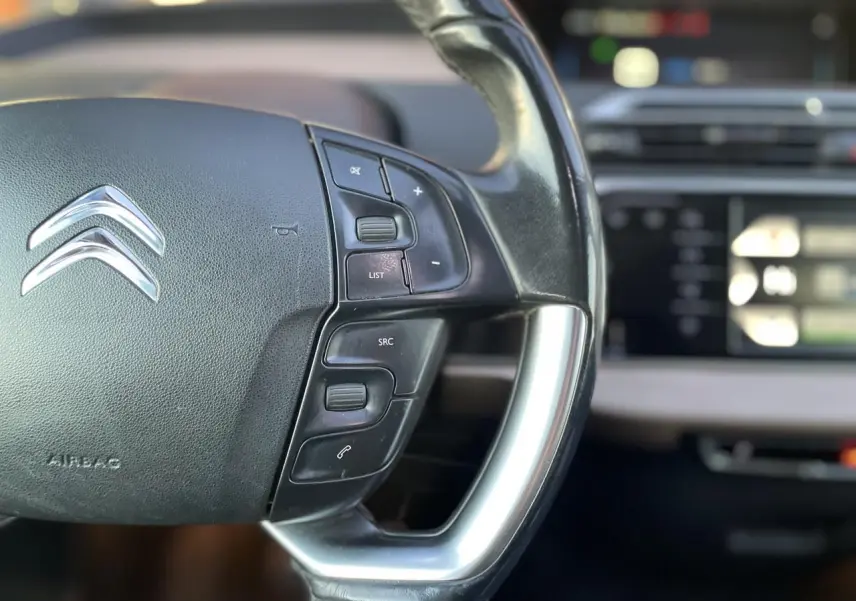 Gros plan sur le volant noir de la Citroën C4 Picasso 2014, avec commandes intégrées et logo chromé visible.