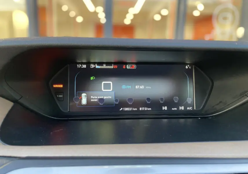 Tableau de bord numérique de Citroën C4 Picasso 2014 affichant la radio FM et l'alerte porte avant gauche ouverte.