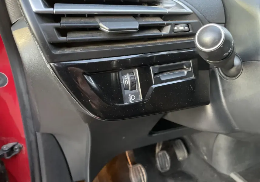 Détail intérieur côté conducteur montrant la commande des phares et la pédale d'embrayage d'une Citroën C4 Picasso rouge foncé.