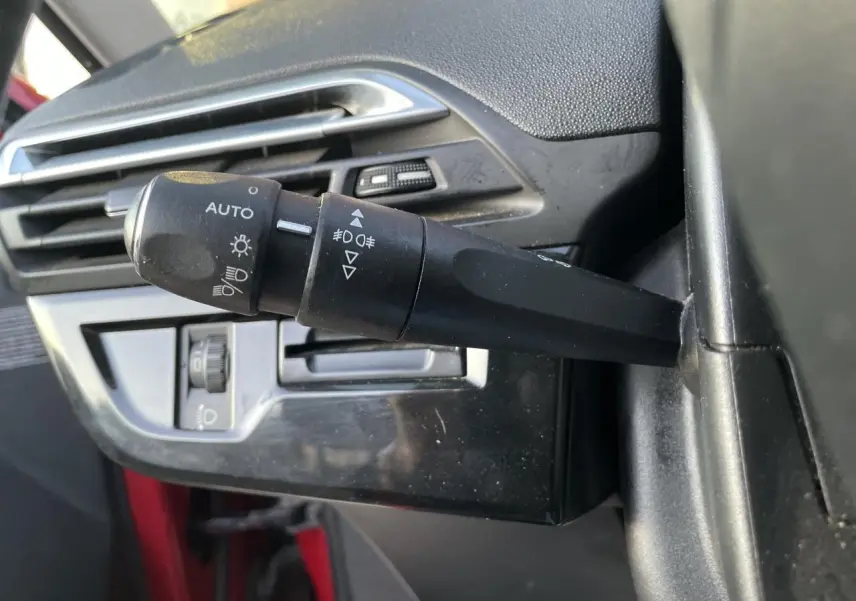 Gros plan sur la commande des phares et antibrouillard à gauche du volant d'un Citroën C4 Picasso rouge foncé.