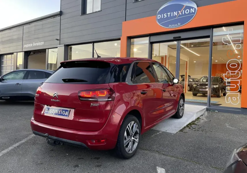 Vue 3/4 arrière droite d'une Citroën C4 Picasso rouge foncé stationnée devant un showroom Distinxion.