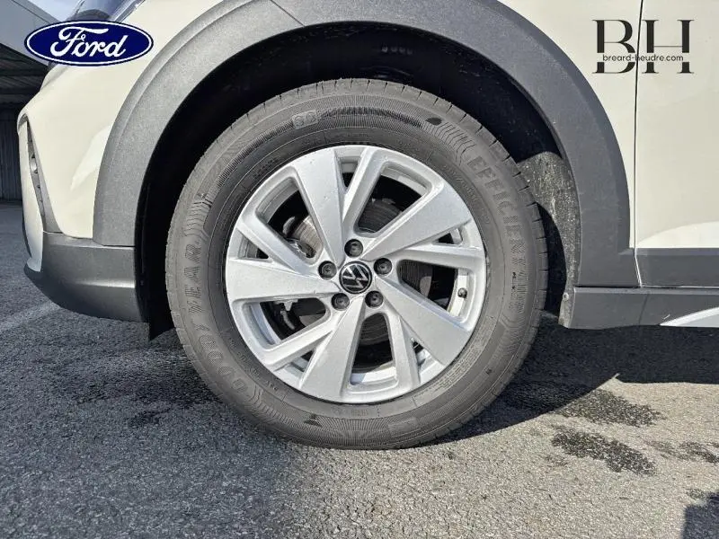 Gros plan sur la roue avant gauche d'un Volkswagen Taigo blanc pur avec jante alu et logo VW central.