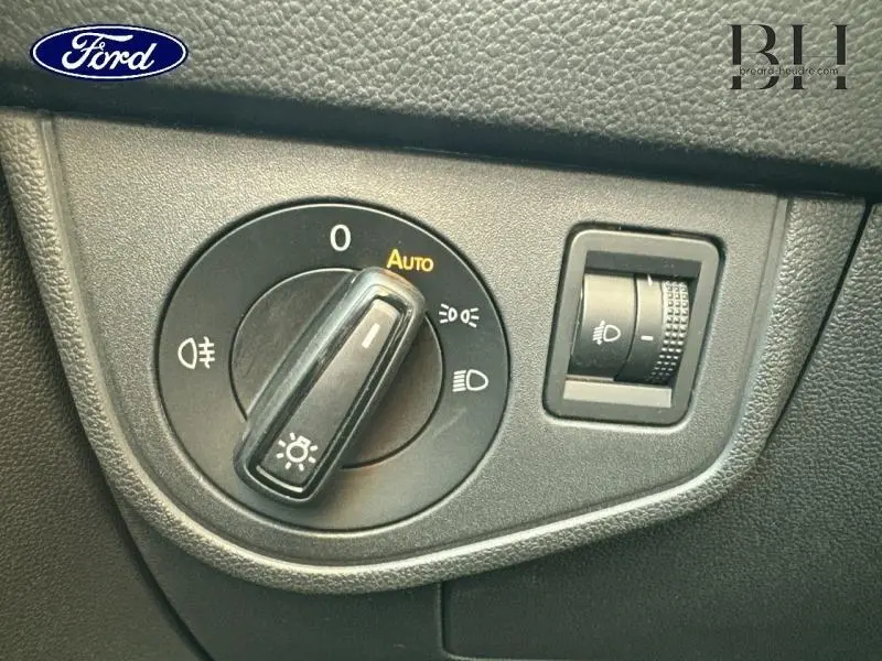 Gros plan sur la commande des phares du Volkswagen Taigo blanc, avec réglage automatique et molette d'ajustement d'intensité.