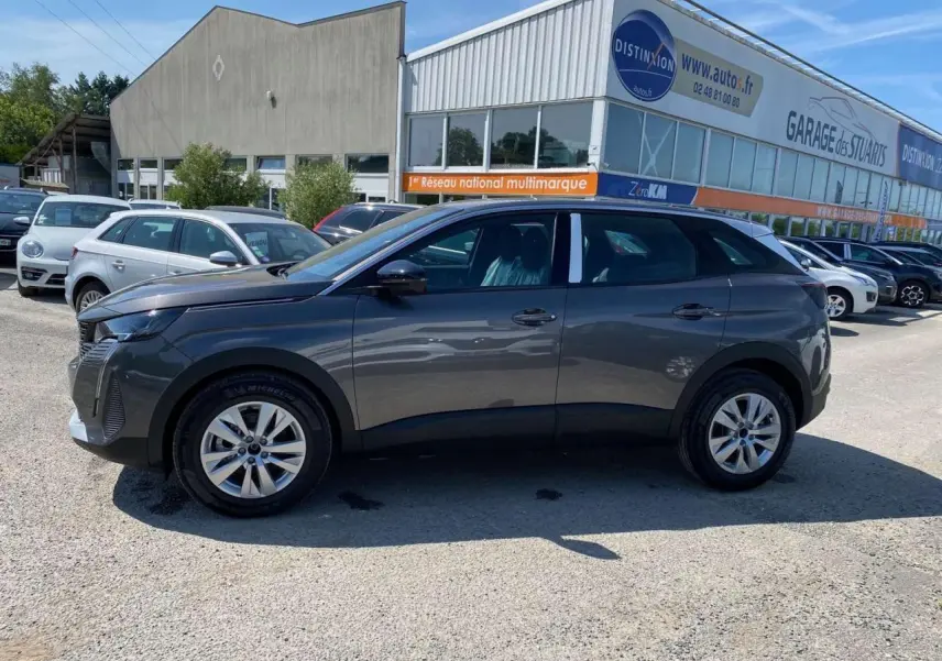 Peugeot 3008 gris platinium vue de profil côté gauche, stationnée devant un garage multimarque en extérieur.