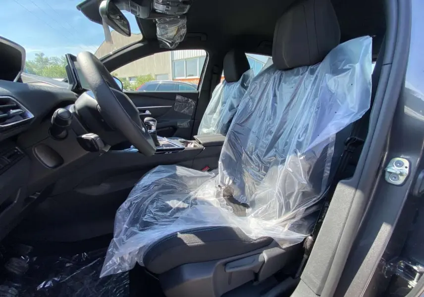 Vue intérieure côté conducteur du Peugeot 3008 gris platinium 2023 avec sièges avant protégés par film plastique.