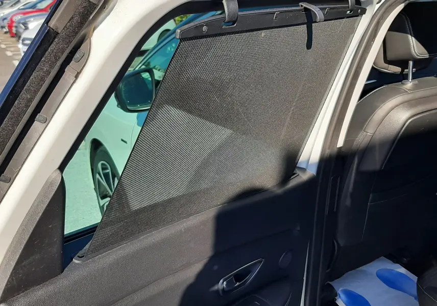 Vue intérieure côté gauche de la Renault Scenic IV blanc nacré avec pare-soleil arrière déployé et sièges noirs.