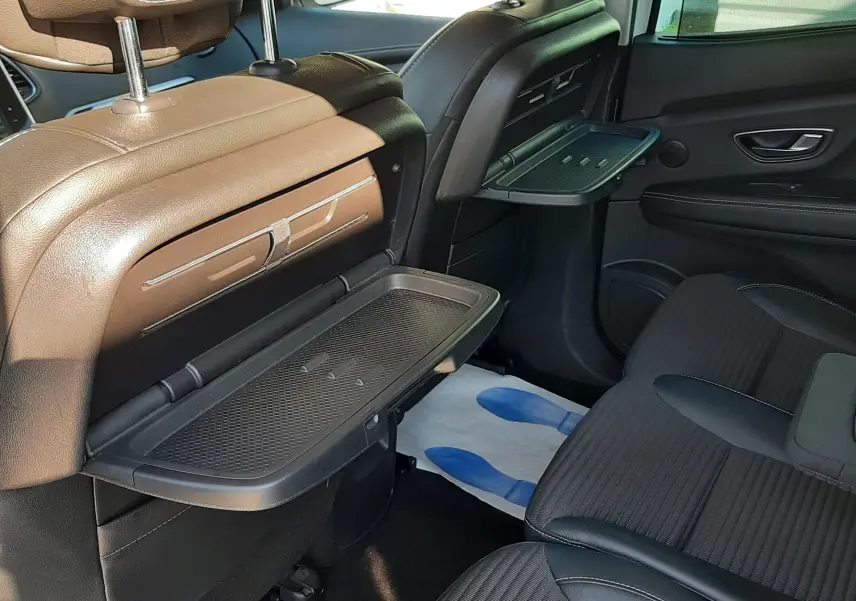 Vue intérieure arrière droite du Renault Scénic IV avec tablettes rabattables sur les dossiers et sièges noirs.
