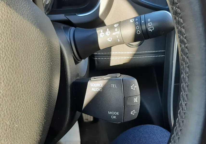 Gros plan sur les commandes audio et essuie-glace à gauche du volant du Renault Scenic IV blanc nacré avec intérieur noir.