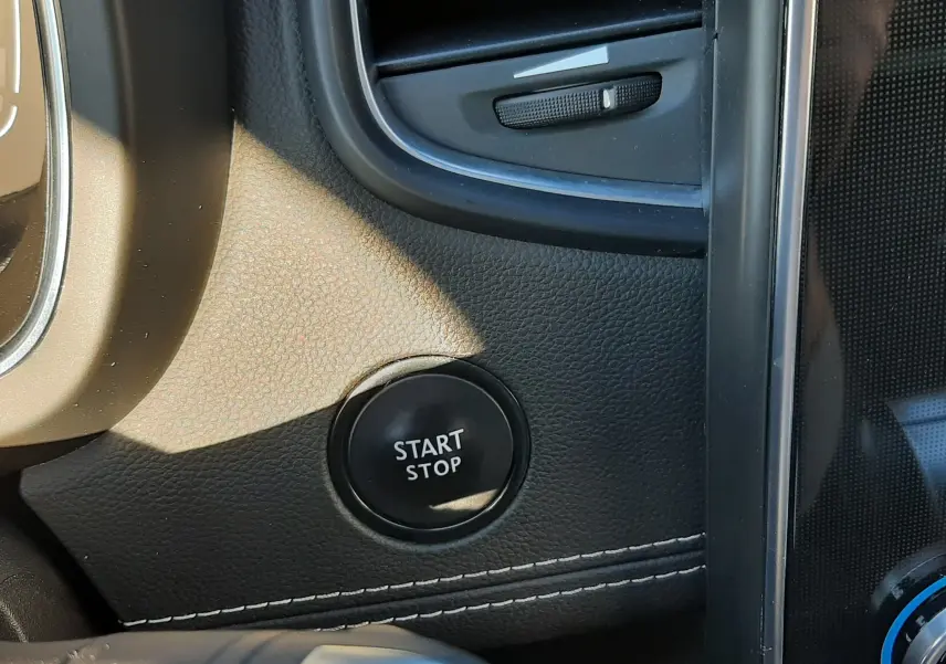 Détail intérieur du tableau de bord noir du Renault Scénic IV avec bouton start/stop et aérateur visible.