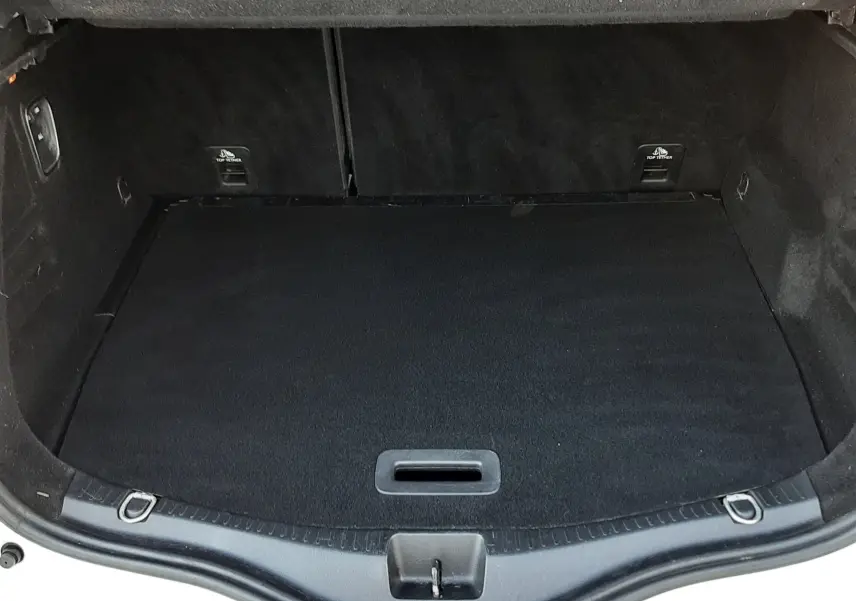 Coffre ouvert vu de l'arrière d'un Renault Scénic IV blanc nacré, intérieur noir et tapis de coffre propre.