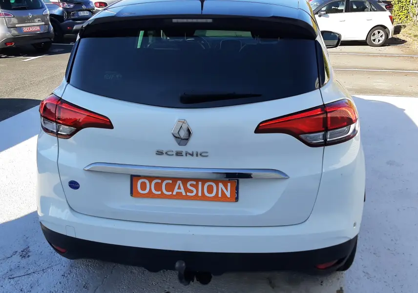 Vue arrière d'un Renault Scénic IV blanc nacré avec toit noir, feux arrière étirés et plaque "OCCASION" orange.