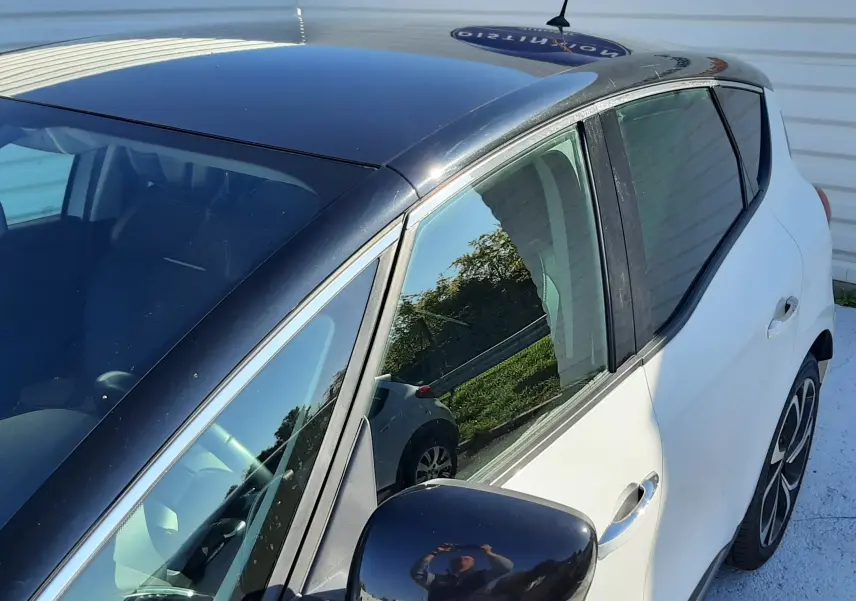 Vue côté gauche avant d'une Renault Scenic IV blanc nacré avec toit noir et rétroviseur noir brillant.